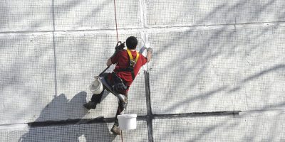 The worker seals hermetically seams of the panel house. Work at height.